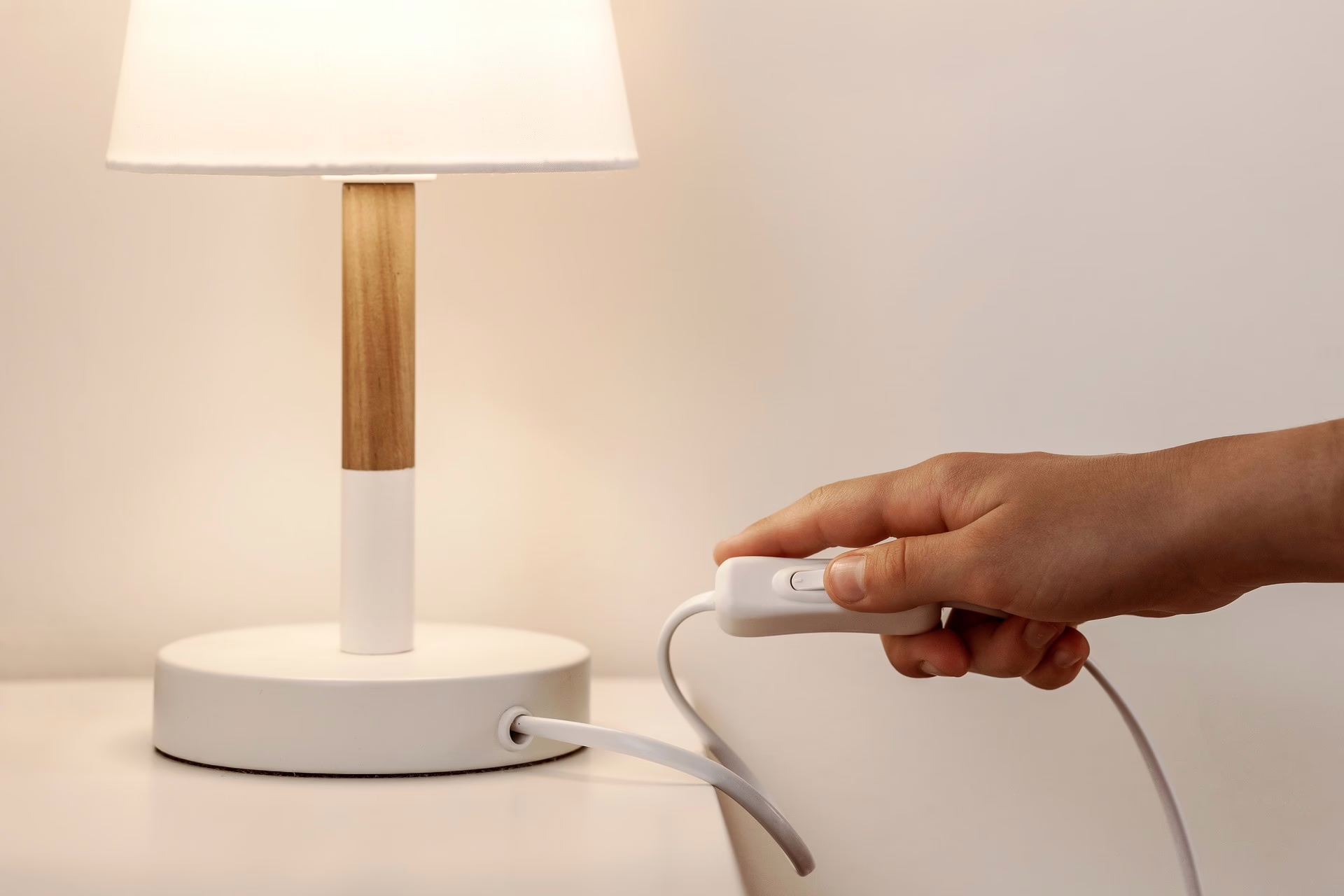 Weiße Lampe mit Holzfuß. Eine Hand ist am Schalter der Lampe.