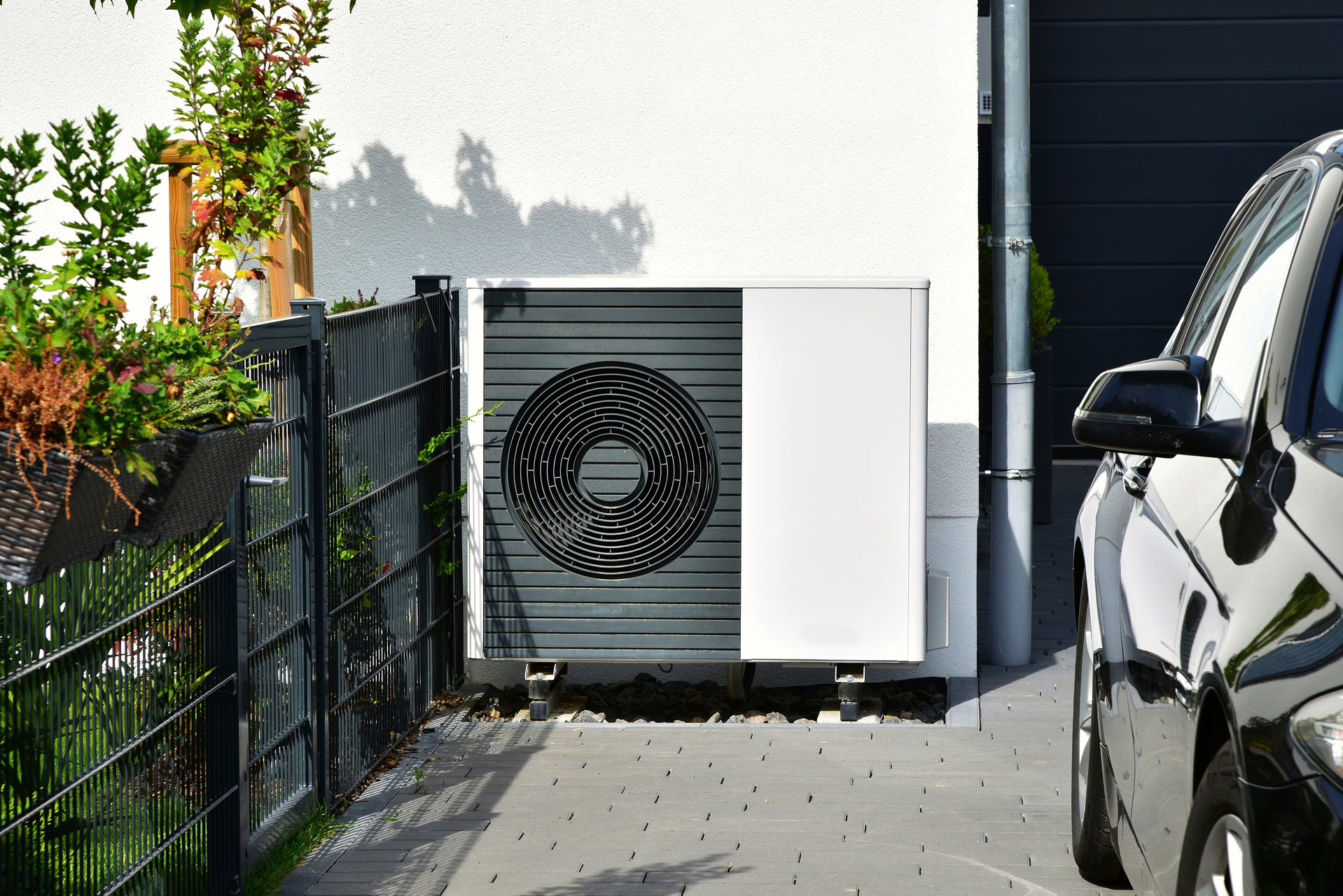 Wärmepumpe steht in einer Garageneinfahrt. Davor steht ein schwarzes Auto.