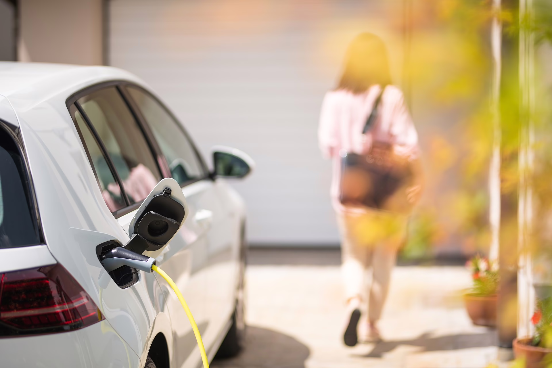 Aufladendes, geparktes Elektroauto mit einer Frau die das Fahrzeug verlässt.