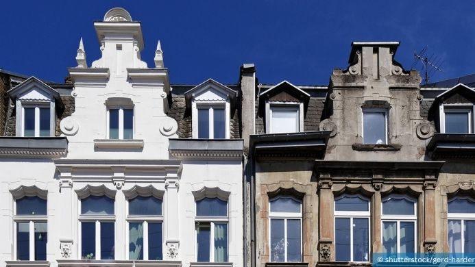 Zwei Altbauten stehen nebeneinander. Das eine ist weiß angestrichen und saniert und das andere unsaniert und hat eine graue Fassade.