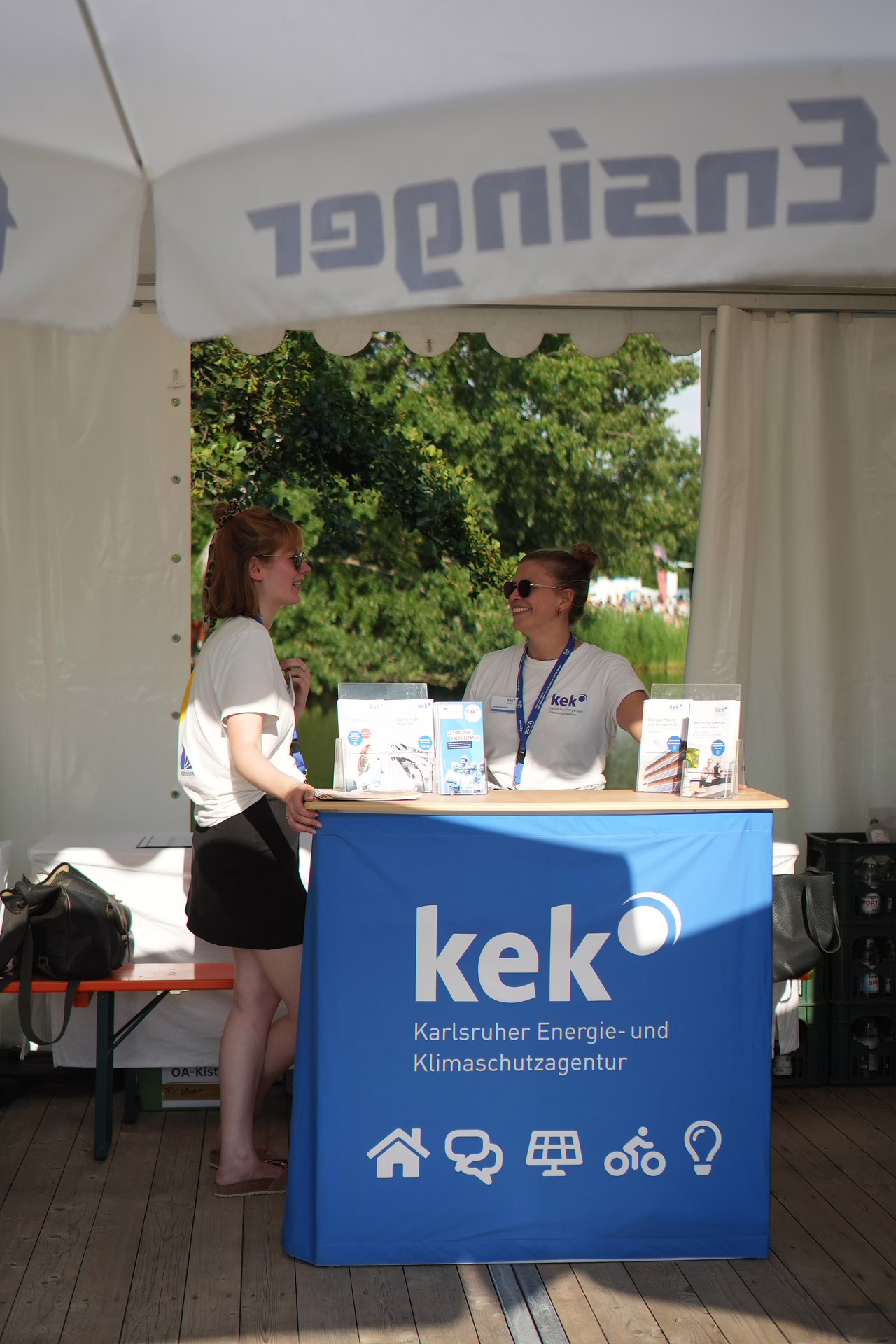 Zwei Mitarbeiterinnen der KEK stehen bei einem Infostand bei "DAS FEST" in Karlsruhe und unterhalten sich.