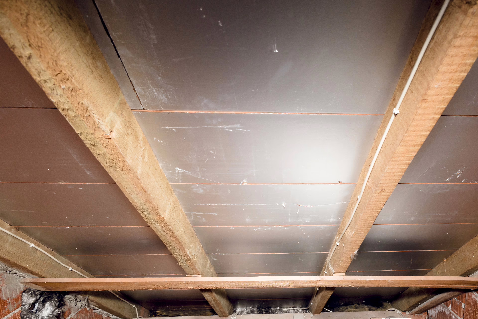 Man sieht die Decke des Hauses. Die Zimmerdecke ist mit Holzbalken ausgestattet.