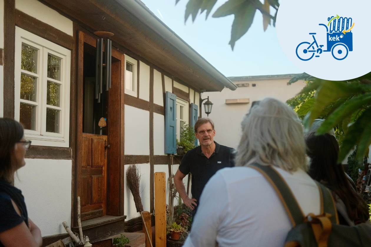 Fachwerkhaus, vor dem mehrere Menschen stehen. Der Hauseigentümer erzählt etwas.
