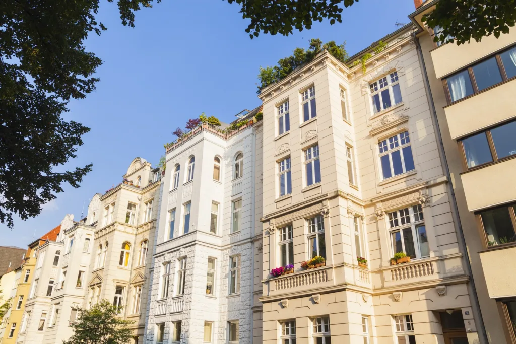 Zu sehen sind mehrere Häuser von vorne. Die Fassaden sind in hellen creme tönen vor einem blauen Himmel.