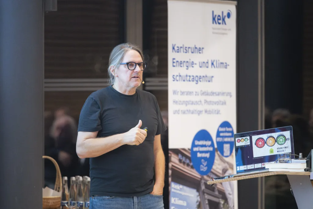 Energiesparkommissar Carsten Herbert hält seinen Vortrag. Im HIntergrund das Roll-up Karlsruher Energie- und Klimaschutzagentur. 