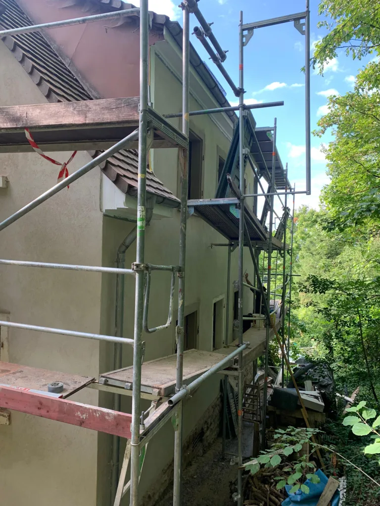 An einer Seite des Hauses ist ei nGrüst. Auf dem Gerüst sind Personen, die die Fassade bearbeiten. 