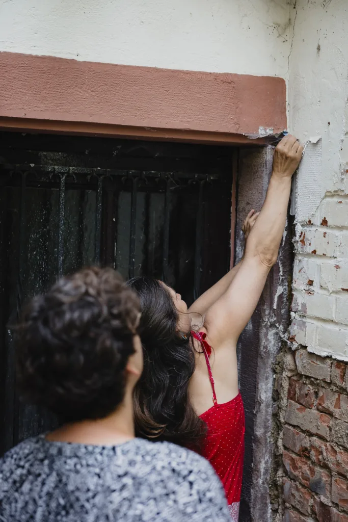 Galina steht an der Tür des Hauses und trägt den Putz an der Fassade auf. 
