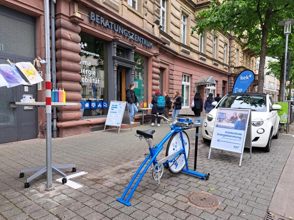 Das Beratungszentrum ist von außen zu sehen. Ein Fahrrad, mit dem Man ein mit Frabe Kust auf Papier machen kann steht vor der Tür. Außerdem ein Schild und Flyerständer.