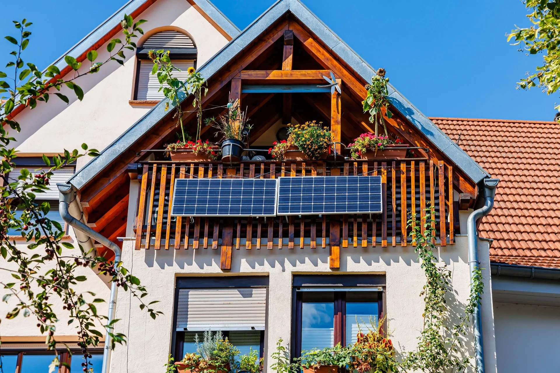 Ein kleiner Balkon aus Holz ist zu sehen. Es wachsen viele Plfanzen darauf. Auch zwei Photovoltaikmodule wurdn am Holzgeländer installiert.