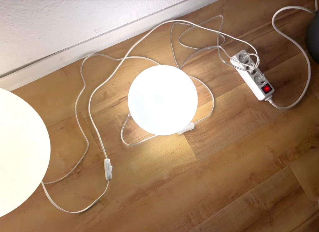 Zwei leuchtende Lampen sind zu sehen. Sie sind in eine Mehrfachsteckdose mit Kippschalter eingesteckt, sodass man sie alle auf einmal ausmachen kann.