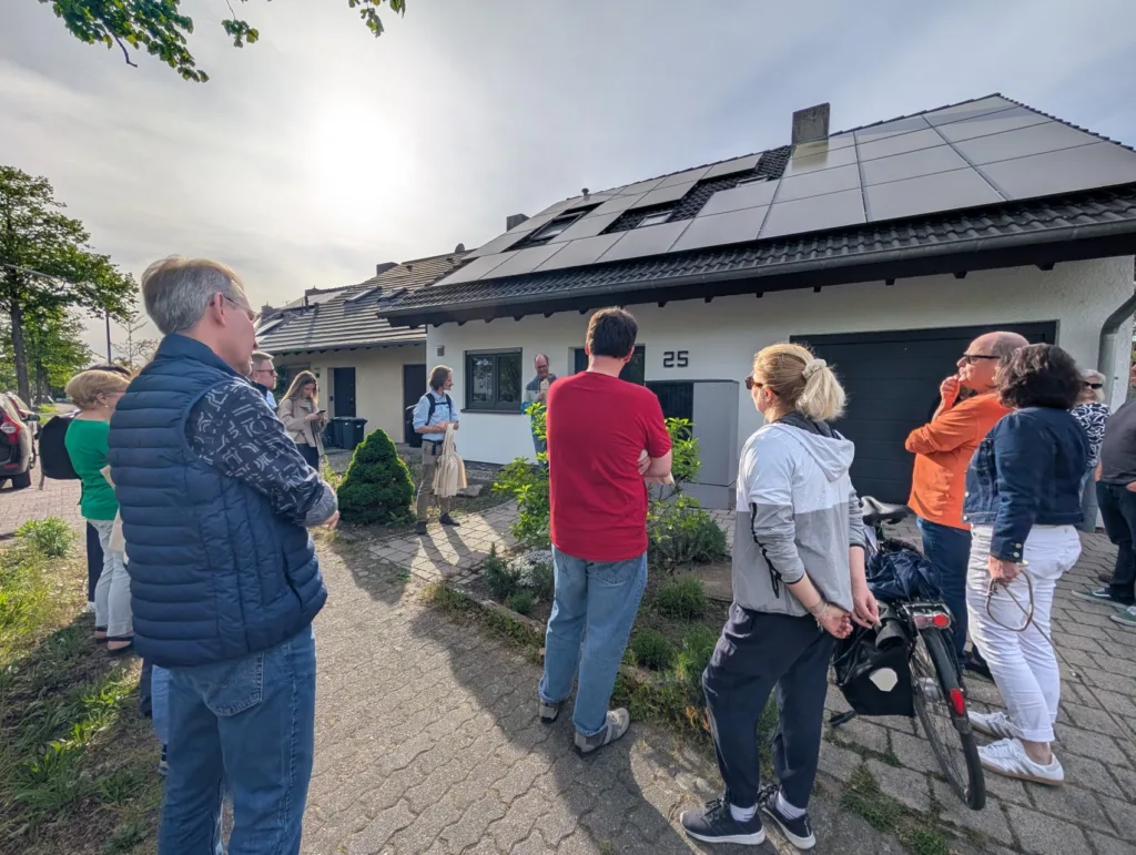 Menschen stehen vor einem Haus, das mit Photovoltaik bedeckt ist. Das Bild ist im Rahmen eines Sanierungsspaziergangs entstanden.