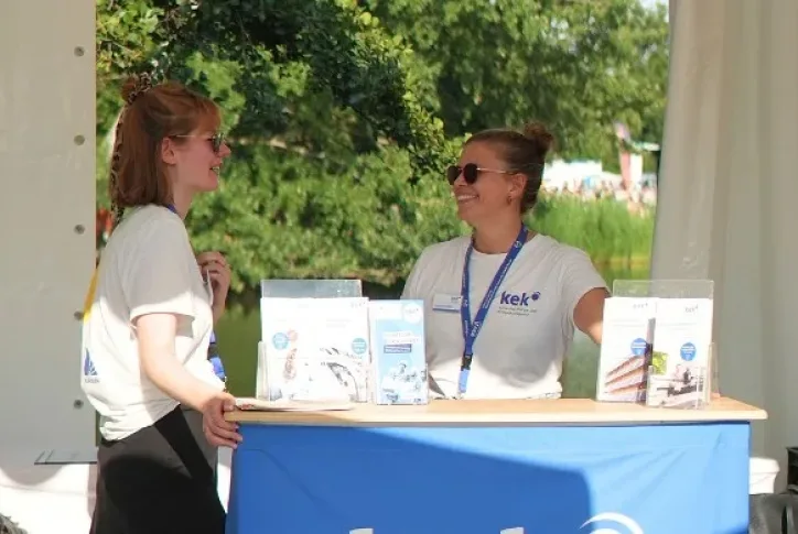 Mitarbeitende der KEK stehen an einem Infostand. Vor ihnen stehen verschiedene Flyer.