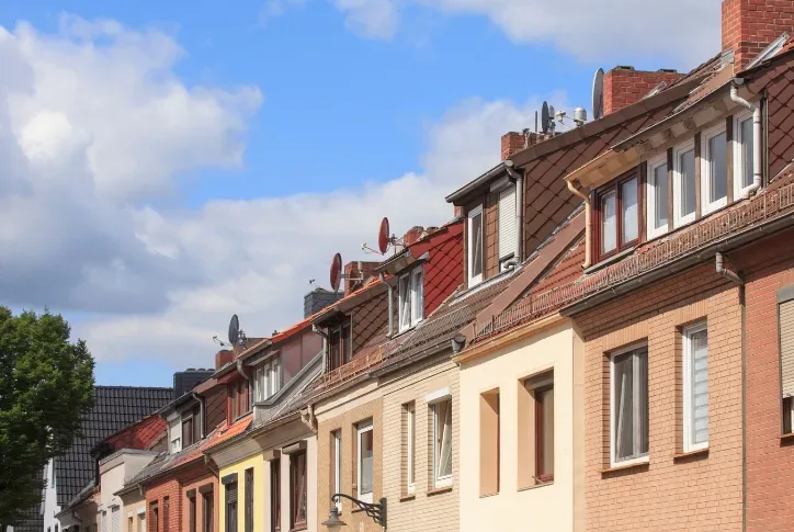 Bild einer Häuserreihe. Der Himmel ist blau und einige Wolken sind zu sehen. Die Häuser sind braun und gelb.