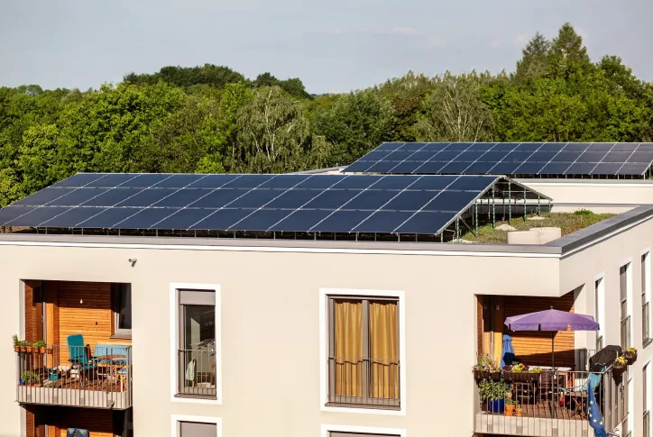 Auf dem Bild ist ein Mehrfamilienhaus mit Flachdach zu sehen. Auf dem Flachdach sind Photovoltaik-Module Installiert.