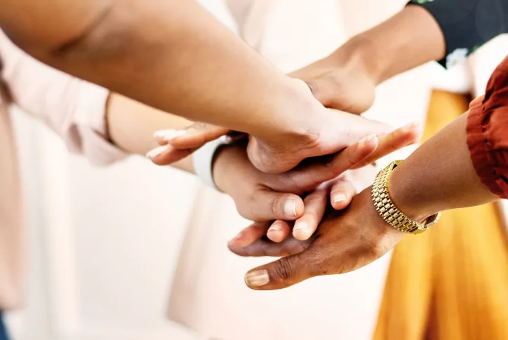 Auf dem Bild ist eine Gruppe Meschen zu sehen, die als Zeichen des erfolgreichen Teamwork ihre Hände aufeinander legen.