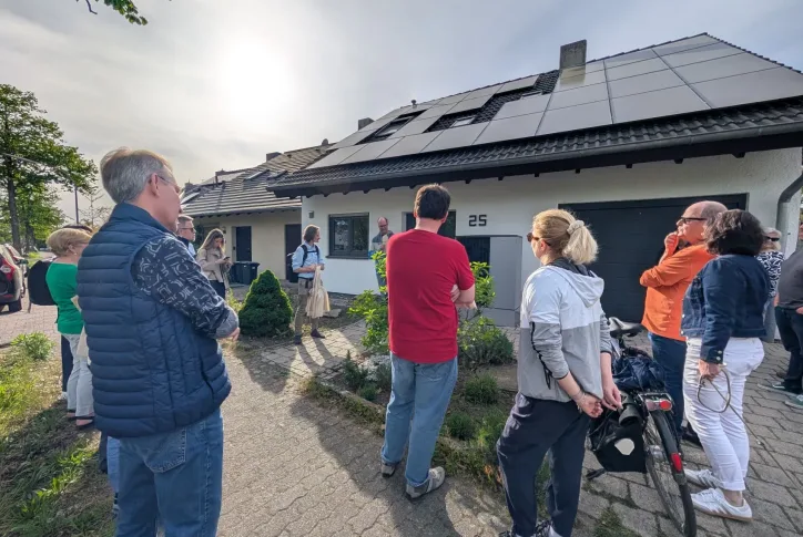 Menschen stehen vor einem Haus, das mit Photovoltaik bedeckt ist. Das Bild ist im Rahmen eines Sanierungsspaziergangs entstanden.