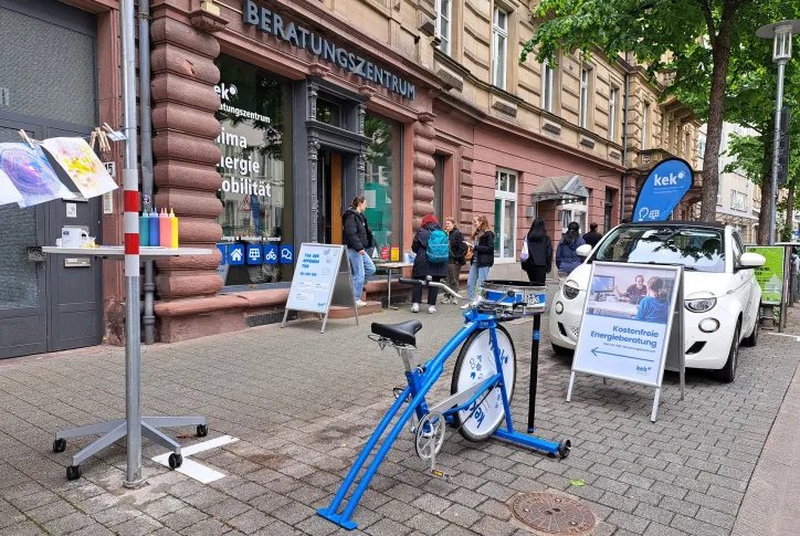 Das Beratungszentrum ist von außen zu sehen. Ein Fahrrad, mit dem Man ein mit Frabe Kust auf Papier machen kann steht vor der Tür. Außerdem ein Schild und Flyerständer.