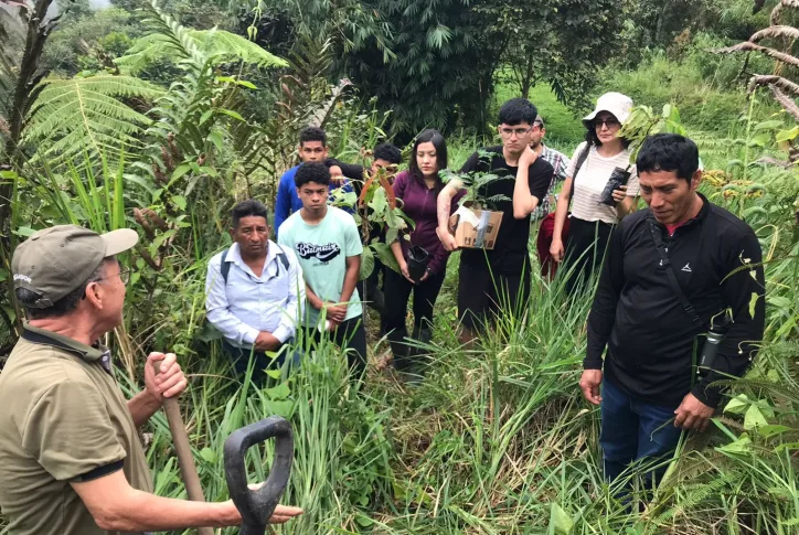 Die Workshopgruppe steht im steilen Gelände m Wald und hört dem Vortragenden zu.